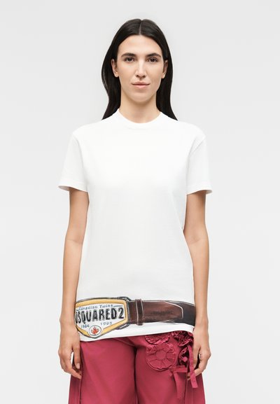 Femme aux longs cheveux foncés portant un t-shirt blanc avec une grande ceinture marron imprimée et le logo DSQUARED2, associé à un pantalon rouge avec un détail floral.