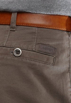 Bruine katoenen broeken hebben een gladde textuur, een metalen knoopsluiting en een bruine leren riem. Een klein 'MEYER'-label is zichtbaar.