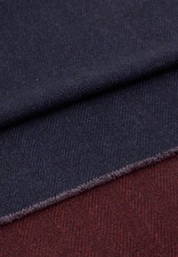 Textilní látka v tmavě námořnické a burgundské barvě s jemným vzorem rybí kosti. Okraje vypadají mírně roztržené, což ukazuje na jemnou texturu.