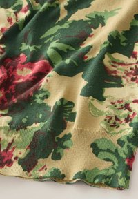 Tissu tricoté avec motif floral en tons rouges, verts et beiges, montrant de doux plis et un tissage texturé.