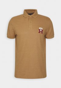 Brązowa koszulka polo z kołnierzykiem, prążkowanymi rękawami oraz małym, haftowanym logo "H" w białym i burgundowym kolorze po lewej stronie klatki piersiowej.