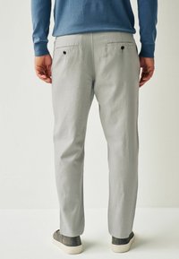 Pantalon gris clair à coupe droite, doté de poches arrière avec fermeture à bouton et d'une texture subtile, porté avec des baskets grises.