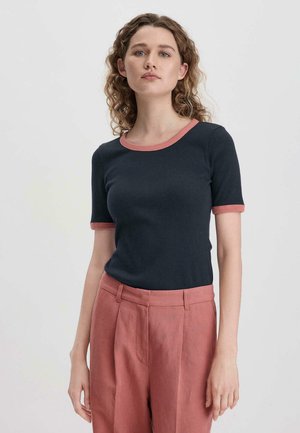Marineblaues, geripptes T-Shirt mit kurzen Ärmeln und pinken Akzenten am Rundhalsausschnitt und an den Ärmeln, kombiniert mit hellrosa, maßgeschneiderten Hosen.
