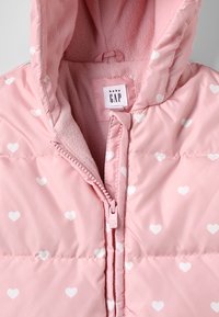 Roze babyjasje met witte hartpatronen, fleece-voering in de capuchon en ritsluiting met een "baby GAP" label.
