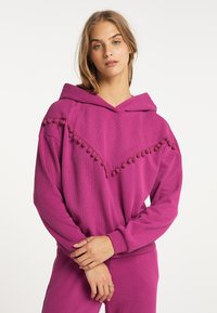 Felpa fucsia realizzata in tessuto morbido, con un bordo a pompon triangolare lungo il colletto, maniche lunghe e una vestibilità comoda con cappuccio.