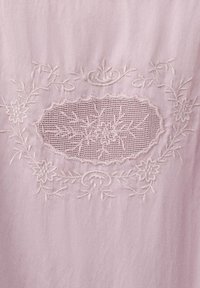 Tissu rose clair avec une broderie florale délicate et un centre ovale en dentelle résille avec des motifs de fleurs et de feuilles.