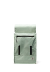 Sac à dos à rabat vert en tissu résistant. Il dispose d'une poche zippée à l'avant, de bretelles noires et d'une petite étiquette logo en bas.