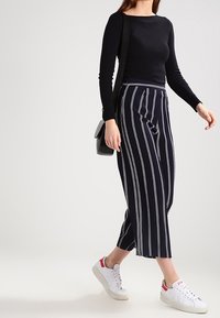 Musta pitkähihaisen paita yhdistettynä tummansinisiin raidallisiin hamehousuihin. Valkoiset tennarit, joissa punaiset yksityiskohdat. Musta olkalaukku täydentää asun.