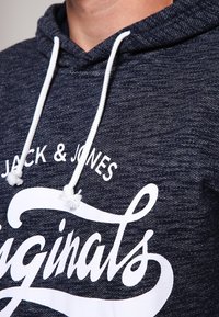 Felpa con cappuccio blu navy a trama con coulisse bianche e grande scritta grafica bianca "originals" con "Jack & Jones" sopra.