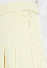 Světlě žlutá sukně s plisováním, hladkým textilním povrchem, širokým pasem a diskrétní boční zip s odpovídajícími taháčky.