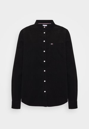 Chemise noire à manches longues avec des boutons blancs, un col et une poche poitrine avec un petit logo rouge, blanc et bleu.