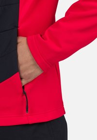Červená a černá bunda s hladkým povrchem. Obsahuje boční kapsu se zipem a přiléhavý střih. Dlouhé rukávy a ploché švy.