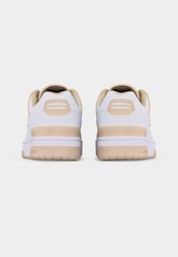 Ζευγάρι λευκών και μπεζ αθλητικών παπουτσιών απεικονίζεται από πίσω πάνω σε απλό ανοιχτό γκρι φόντο.