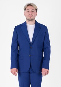 Abito blu con rever a punta, due bottoni e tasche laterali. Vestibilità sartoriale, abbinato a una t-shirt bianca semplice sotto.