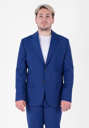 Abito blu con rever a punta, due bottoni e tasche laterali. Vestibilità sartoriale, abbinato a una t-shirt bianca semplice sotto.