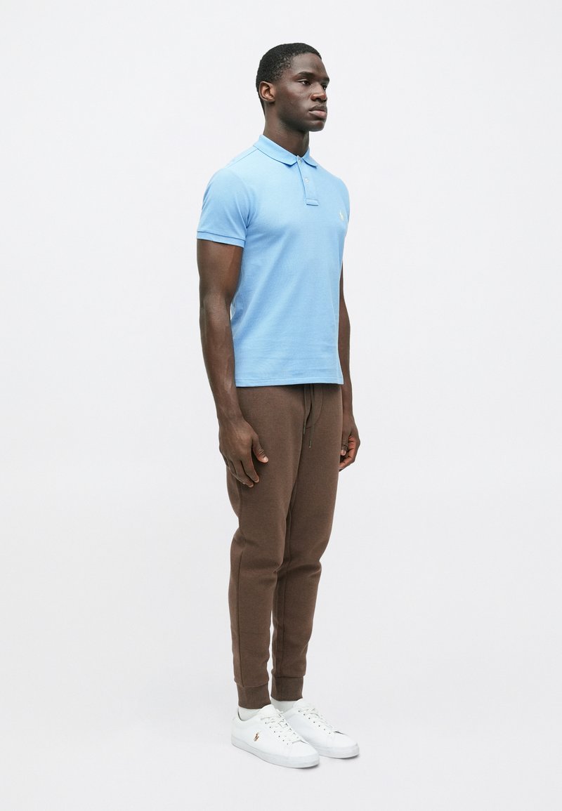 Lichtblauwe poloshirt met een kraag, gecombineerd met bruine joggingbroek en witte sneakers. De outfit heeft een slim fit en een eenvoudig ontwerp.