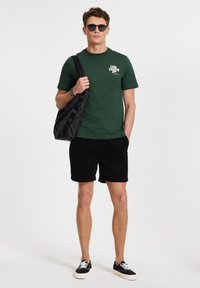 Zelené bavlnené tričko s textom "Like Locals Do", čierne kordové šortky, čierna crossbody taška a čierne slnečné okuliare. Neformálny outfit so teniskami.