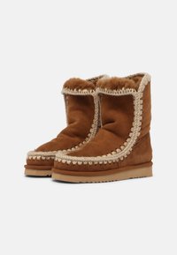 Bottes en daim marron avec doublure en peluche, bordure tressée décorative et texture douce. Avec une semelle plate et un design à bout rond.