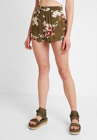 Shorts à fleurs vert olive avec une coupe décontractée et une taille élastique, associés à des sandales à plateforme vert olive avec plusieurs brides.
