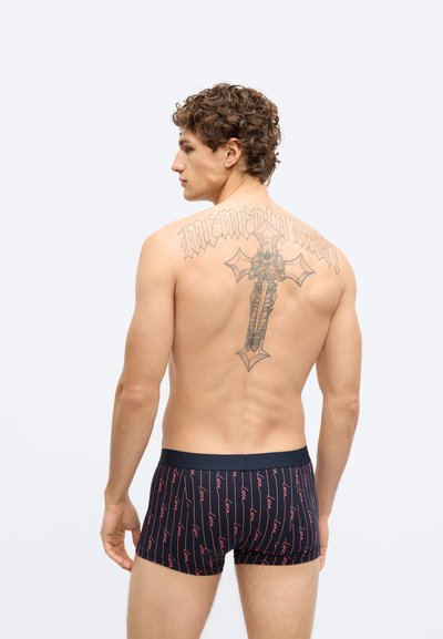 Tengerészkék boxeralsó piros "love" feliratos mintával, kényelmesen simuló szabással és puha anyagból. A modellen látható egy hátat díszítő tetoválás.