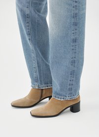 Tan suede ankle boots with a square toe, a black block heel, and a zipper detail, paired with light blue straight-leg jeans.
