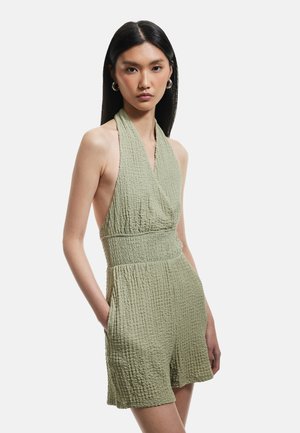 Mono corto verde claro con cuello halter, fabricado en una tela texturizada, con cintura ajustada y bolsillos. Presenta un corte holgado y un diseño casual.
