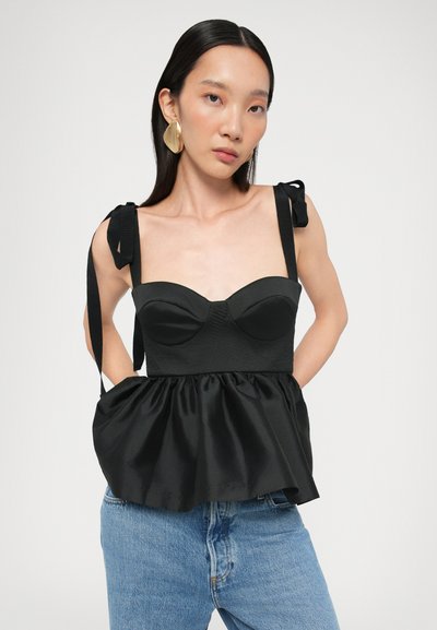 Black peplum top with structured bodice, adjustable shoulder ties, and satin finish. Paired with blue denim jeans.