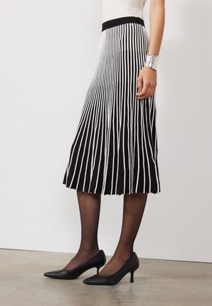 Svart og hvit plisserte skjørt med vertikale striper, med en svart midje. Modellen har på seg svarte hæler og gjennomsiktige svarte strømpebukser.