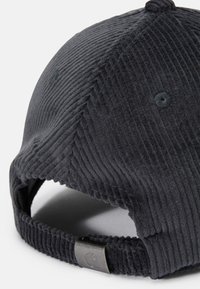 Gorra de pana negra con una superficie texturizada, visera curvada y una correa ajustable con un cierre de metal en la parte trasera.