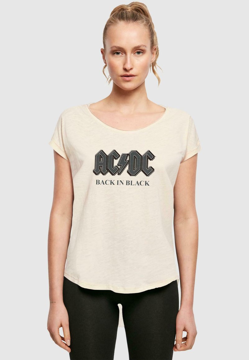 Cremefarbenes T-Shirt mit Rundhalsausschnitt und aufgerollten Ärmeln. Mit schwarzem AC/DC-Logo und dem Text "BACK IN BLACK" auf der Vorderseite bedruckt.