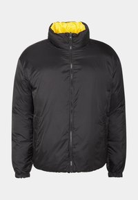 Svart vadderad jacka med hög krage, gul innerfoder, frontdragkedja och elastiska manschetter. Har en mjuk yta och minimalistisk design.