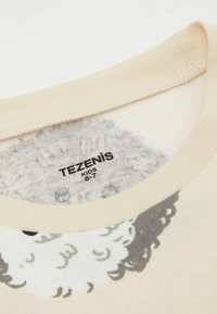 Beżowy t-shirt bawełniany z okrągłym dekoltem i graficznym nadrukiem owcy w odcieniach szaro-białych, z widoczną metką "TEZENIS KIDS 6-7".