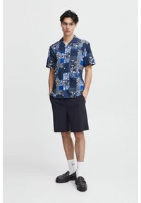 Trumpo rankovės tamsiai mėlyna mygtukų marškinėlių chemise su lopymo dizainu, kuriame derinamos gėlių, taškelių ir languotų raštų. Suderinta su tamsiais šortais ir juoda avalyne.