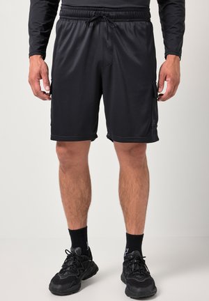 Mand iført sorte atletikshorts, sort langærmet trøje, sorte sokker og sorte sneakers, der står mod en ensfarvet baggrund.