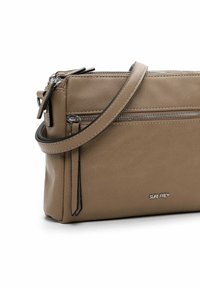 Tan leather crossbody bag with silver zipper accents, single strap, and logo. Features a textured finish and compact rectangular shape.
