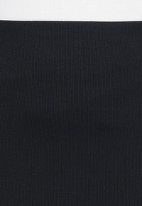 Tessuto nero a coste con una texture che presenta linee verticali, formando un design aderente. La parte superiore è in un tessuto bianco a contrasto, piatto.