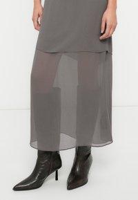 Γκρι πολυεπίπεδο φόρεμα με διαφανές κάτω μέρος. Συνδυασμένο με καφέ σκούρες μπότες με ψηλό τακούνι και μυτερή μύτη, με φερμουάρ στο πλάι.