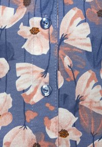 Kvetinová košeľa na gombíky s modrým pozadím, veľkými ružovými a hnedými kvetmi, jemnou textúrou a kovovými gombíkmi.