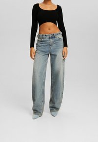 Svart ribbad långärmad crop top som är nätt matchat med högmidjade, ljusblå vida jeans och spetsiga klackar. Slät tyg, avslappnad passform.