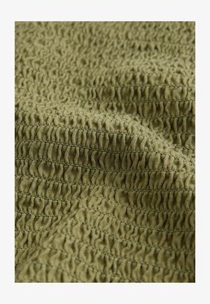 Texturerad olivgrön tyg med samlade veck, som kännetecknas av ett mjukt, något stretchigt material. Visar detaljerade sömnadsmönster.