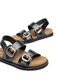 Sandalias de cuero negro con dos correas anchas ajustables y hebillas doradas. Plantilla de corcho con suela de goma negra y tachuelas de acento doradas.
