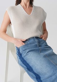 Haut sans manches à col en V en maille côtelée crème associé à une jupe en denim bleu clair avec un panneau latéral bleu foncé.