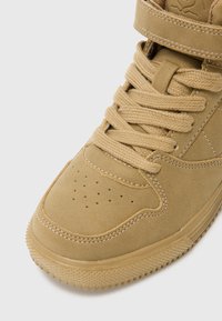 Kreemilt suede-stiilis tennisetossid, millel on pehmendustega kaelus, perforeritud varvas, lame pael ja kummist tald, millel on tekstuuriga mustripattern.