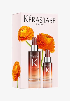 Kérastase Nutritive Haarserum-Duo mit Pumpflaschen in verlaufender bernsteinfarbener Verpackung, aufgestellt vor einer pinken Schachtel mit leuchtend orangefarbenen Blumen.