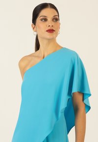 Abito asimmetrico senza maniche in tessuto di un vivace blu, caratterizzato da morbide drappeggiature e una texture liscia, completato da un collo rotondo.