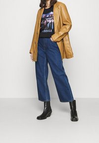 Ruskohvit leather oversized blazer, must grafiikaga t-särk, kõrge vöökohtadega sinised denim lai jalad teksad ja mustad pahkluu saapad, millel on väike konts.