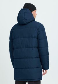 Mornarska puffer jakna s prilagodenim kapu, s prešanim dizajnom, glatkom teksturom i dugim rukavima. Duljina doseže sredinu bedara.