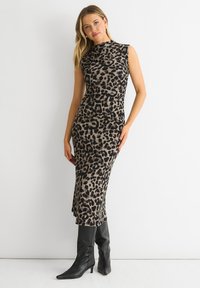 Leopard print dress in tan and black, sleeveless design, fitted silhouette, falls to mid-calf, paired with knee-high black boots.