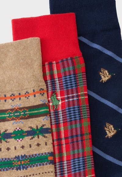 Trois chaussettes colorées à motifs comprenant des formes géométriques, un motif à carreaux rouge avec un cheval vert et des canards sur un fond bleu marine.