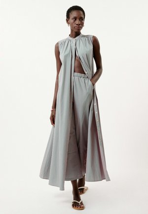 Robe sans manches à rayures avec une fente haute, fabriquée en tissu léger. Elle comporte une fermeture à boutons et une jupe évasée et fluide. Sandales décontractées.